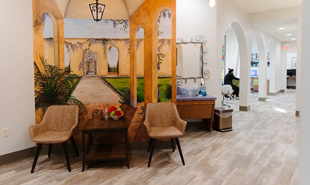 An indoor waiting area designed with wooden pergolas, comfortable armchairs, and potted plants.