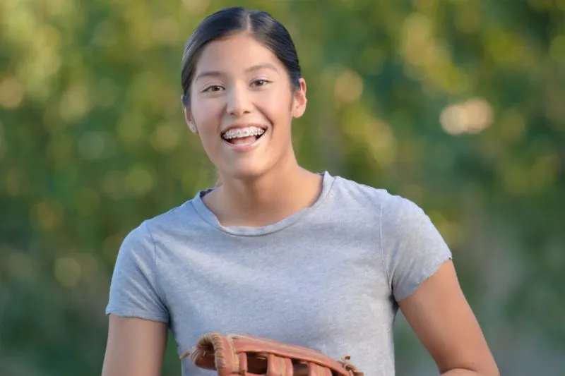 A young woman smiling outdoors in a grey t-shirt, looking healthy and confident.