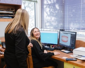 Two women in a dental office looking at a computer screen together and smiling.