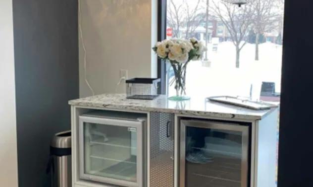 A clean, white counter area in a dental office featuring a glass-door mini-fridge and a vase of flowers.