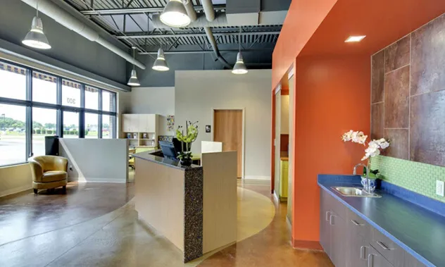 A sleek dental office reception desk featuring warm wood tones, orange accent walls, and bright lighting.