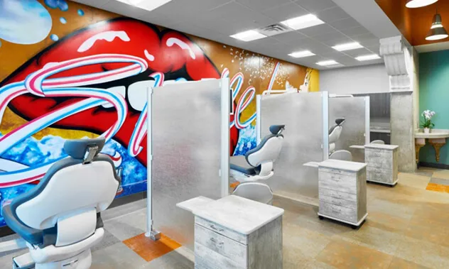 A high-tech orthodontic treatment area featuring glass dividers and a vibrant, colorful mural on the back wall.