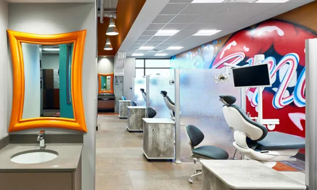 A view down a modern orthodontic clinical hallway featuring a patient sink with a bright orange mirror and treatment stations in the background.