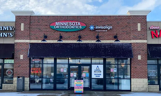 A front-facing view of the orthodontic office located in a brick commercial building with large glass windows and black awnings.
