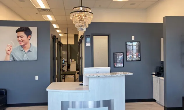 A bright, clean reception area with a white desk, grey walls, and a decorative chandelier.