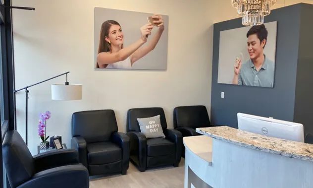 A small, modern waiting area with black leather armchairs and framed photos of smiling patients on the walls.