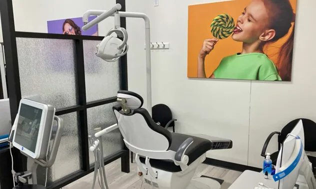 A private dental treatment room with a white chair, clinical equipment, and a large colorful photo of a child on the wall.
