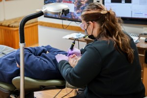 A dental assistant or technician with long hair works on a dental appliance at a laboratory station.