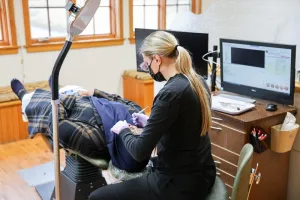 A dental professional in a black uniform working on a patient while referring to digital scans on multiple monitors.