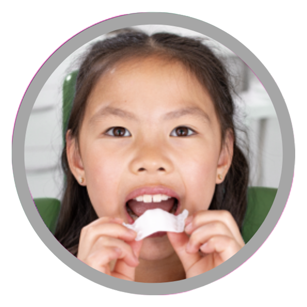 A circular portrait of a young girl holding a white dental appliance or mouthguard in her hands.