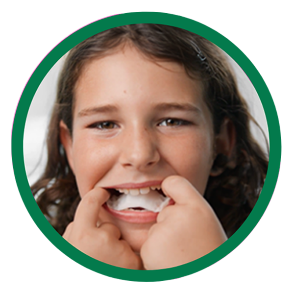 A circular portrait of a girl smiling while holding a white dental tray or aligner up to her teeth.