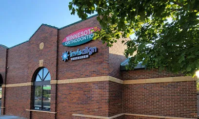 A low-angle shot of a classic red brick building showing the colorful Minnesota Orthodontics and Invisalign provider signs.