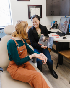 A dentist and a patient sitting in a consultation room, reviewing information on a tablet together.