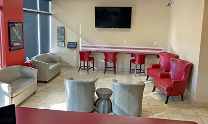 A bright lobby featuring red and grey seating, a high-top counter with stools, and a wall-mounted television.