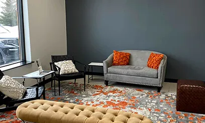 A stylish waiting area with a grey sofa, orange pillows, a tufted bench, and a modern patterned rug.