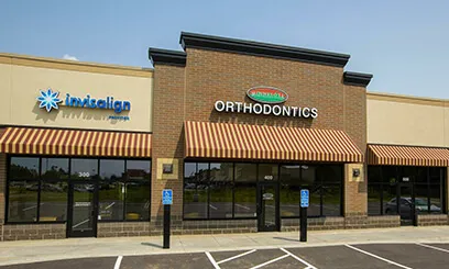 The exterior of an orthodontic office located in a modern retail strip with large glass windows.