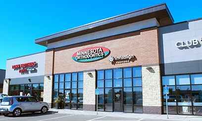 A modern exterior view of a Minnesota Orthodontics location in a commercial retail building with large glass windows.