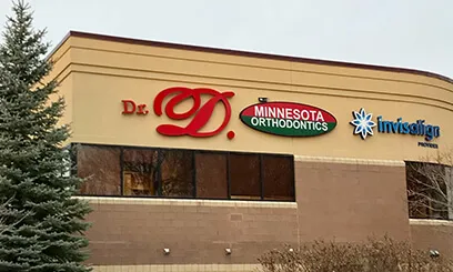 An exterior view of a tan building featuring large signs for Dr. D, Minnesota Orthodontics, and Invisalign.