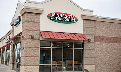 A storefront location for Minnesota Orthodontics in a light-colored brick building with red awnings above the windows.