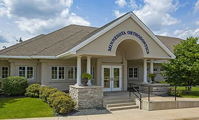 The exterior of a large, traditional-style Minnesota Orthodontics building featuring white columns, a gabled roof, and a prominent arched entryway.