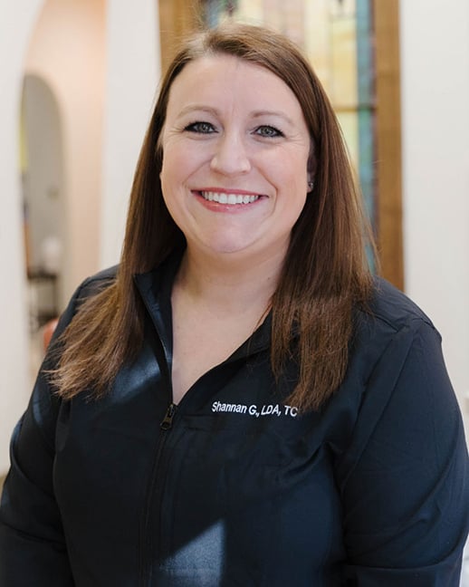 A headshot of Shannan G. &ndash; Treatment Coordinatorwith dark hair wearing a black professional scrub top.