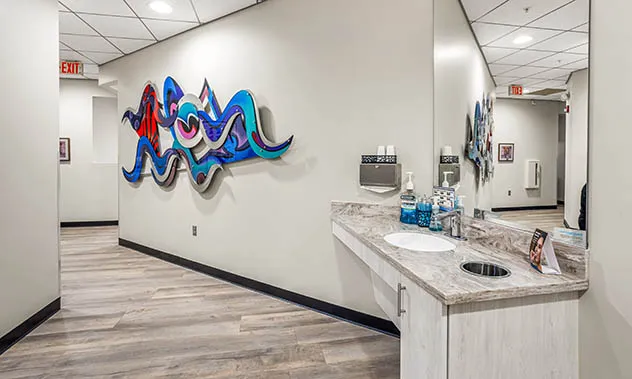 A view of a dental office hallway featuring a patient sink area and a large, colorful piece of modern wall art.