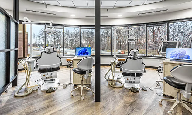 Several dental treatment stations positioned in front of floor-to-ceiling windows overlooking a wooded area.