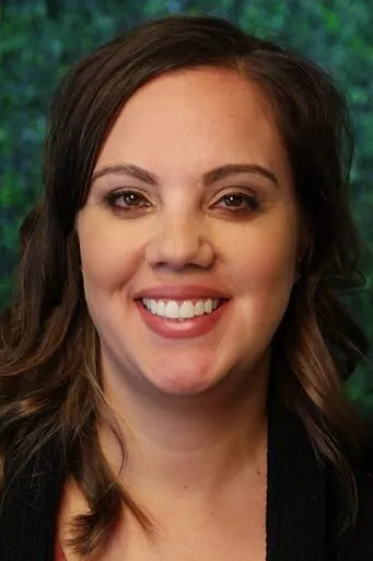 A headshot of Jessica S. – Treatment Coordinator with brown wavy hair smiling against a green textured background.