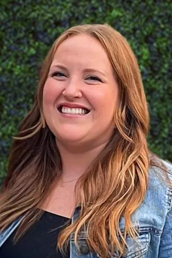 Kailey S. – Treatment Coordinator smiling with long red hair wearing a denim jacket, posed against a green leafy background.