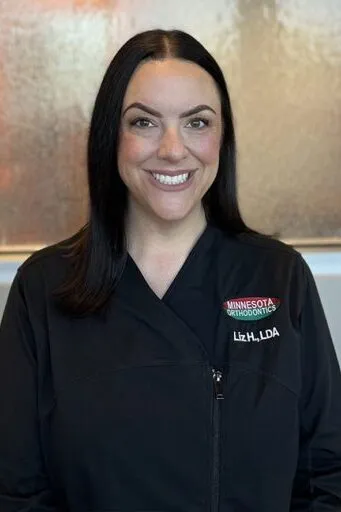 A headshot of Liz H. &ndash; Treatment Coordinator with dark hair wearing a black professional dental scrub top.